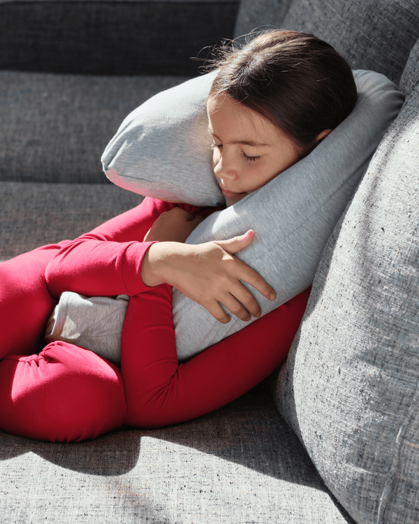 Child relaxing on a couch while hugging the Calmily Perfectly Weighted Pillow for calming deep pressure support and comfort.